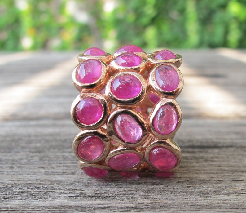 May include: A rose gold ring with multiple rows of pink oval-shaped gemstones.