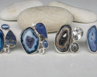 May include: Four silver rings with blue agate and lapis lazuli stones. The rings are set with clear quartz crystals.