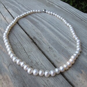 May include: A white pearl necklace with a silver clasp. The necklace is lying on a wooden surface.