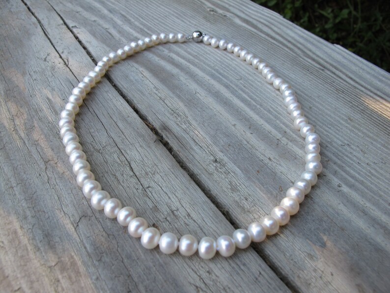 May include: A white pearl necklace with a silver clasp. The necklace is lying on a wooden surface.