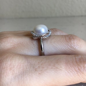 May include: A silver ring with a white pearl and a diamond-encrusted band.