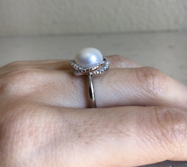 May include: A silver ring with a white pearl and a diamond-encrusted band.