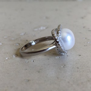 May include: A silver ring with a large white pearl set in a silver halo with small clear stones.