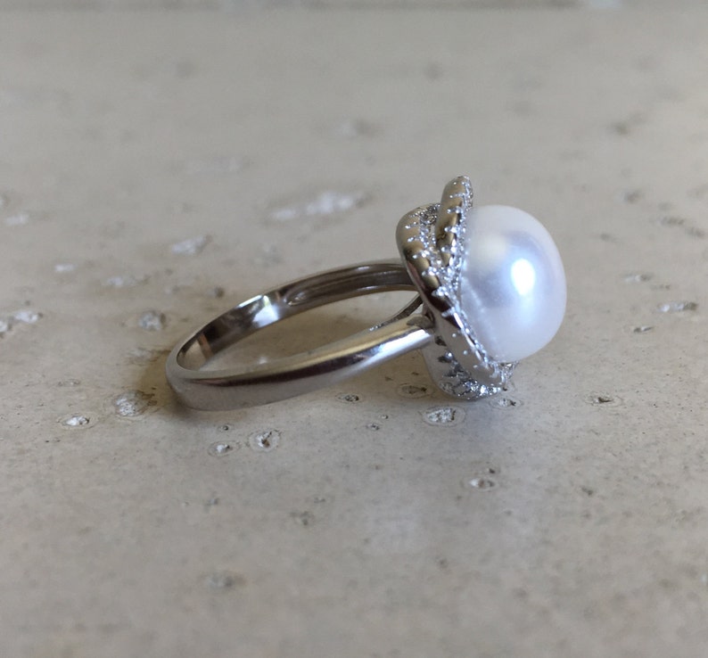 May include: A silver ring with a large white pearl set in a silver halo with small clear stones.