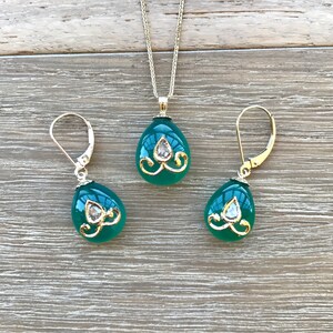 Op de afbeelding: Een groene edelsteen ketting met hanger en bijpassende oorbellen met gouden accenten en heldere strass steentjes. De traanvormige stenen zijn gezet in goud en hebben een delicaat bloemmotief.