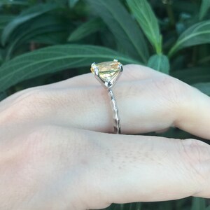 May include: A silver ring with a yellow gemstone set in a prong setting. The ring has a twisted band.