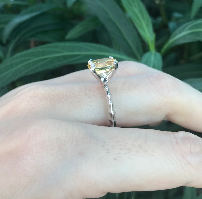May include: A silver ring with a yellow gemstone set in a prong setting. The ring has a twisted band.