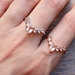 May include: Two gold rings with a row of pear-shaped gemstones. The rings are worn on the index and middle fingers of a hand.