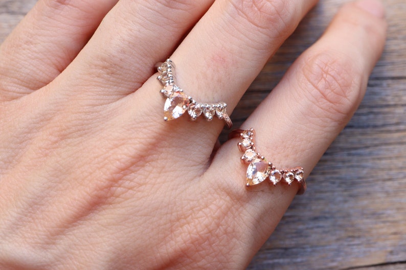 May include: Two gold rings with a row of pear-shaped gemstones. The rings are worn on the index and middle fingers of a hand.