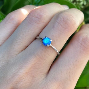 May include: A silver ring with a blue opal gemstone. The ring is on a finger.