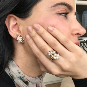 May include: A pair of gold earrings and a gold ring with white pearls and blue gemstones. The earrings and ring are clustered with pearls and gemstones.