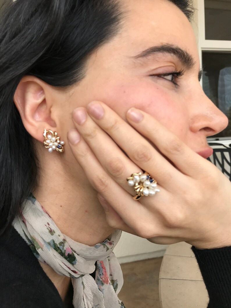 May include: A pair of gold earrings and a gold ring with white pearls and blue gemstones. The earrings and ring are clustered with pearls and gemstones.