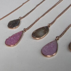 May include: Five gold necklaces with teardrop-shaped pendants. The pendants are made of clear quartz with a sparkly, crystalline texture. The quartz is in shades of pink and gray.