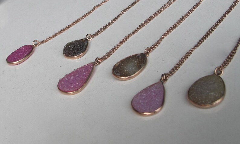 May include: Five gold necklaces with teardrop-shaped pendants. The pendants are made of clear quartz with a sparkly, crystalline texture. The quartz is in shades of pink and gray.