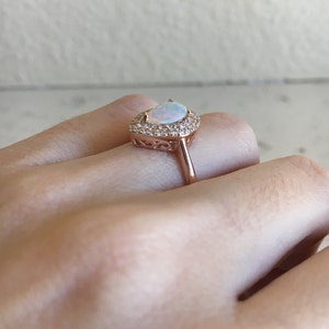 May include: A rose gold ring with a pear-shaped opal gemstone surrounded by a halo of smaller clear stones.