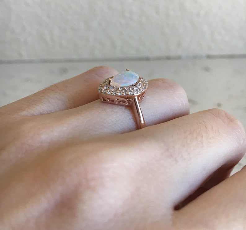 May include: A rose gold ring with a pear-shaped opal gemstone surrounded by a halo of smaller clear stones.