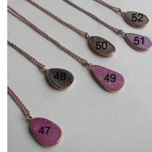 May include: Five silver necklaces with teardrop-shaped pendants. The pendants are made of different types of agate and are numbered 47 through 52.
