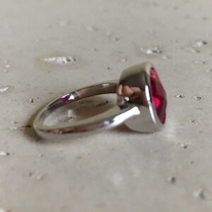 May include: A silver ring with a large, red, faceted gemstone.
