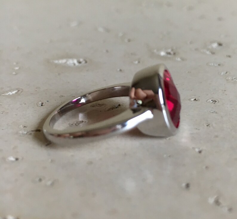 May include: A silver ring with a large, red, faceted gemstone.