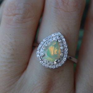 May include: A pear-shaped opal ring with a double halo of clear cubic zirconia stones set in silver.