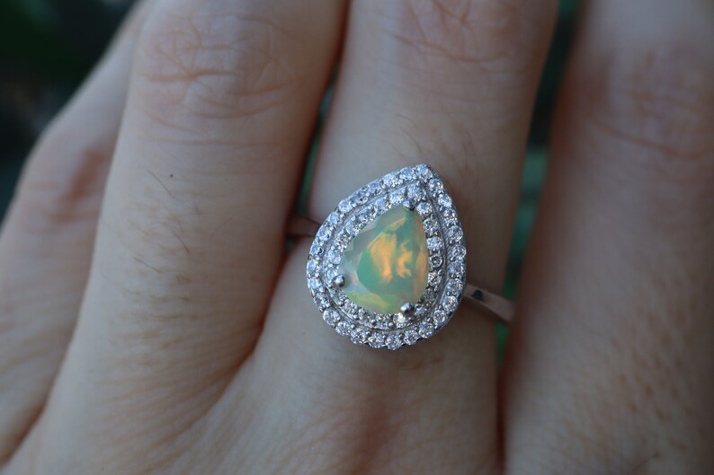 May include: A pear-shaped opal ring with a double halo of clear cubic zirconia stones set in silver.