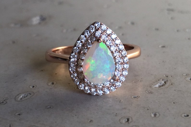 May include: A pear-shaped opal ring set in rose gold with a double halo of clear round stones.