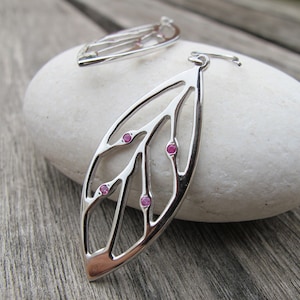May include: Silver earrings with a delicate leaf design and pink gemstones. The earrings are dangle style and have a hook closure.