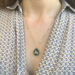 Op de afbeelding: Een gouden ketting met een groene edelsteen hanger. De hanger heeft de vorm van een traan en heeft gouden accenten.