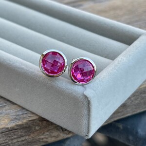 Puede incluir: Un par de pendientes de bot&oacute;n de plata con piedras preciosas facetadas de color rosa.