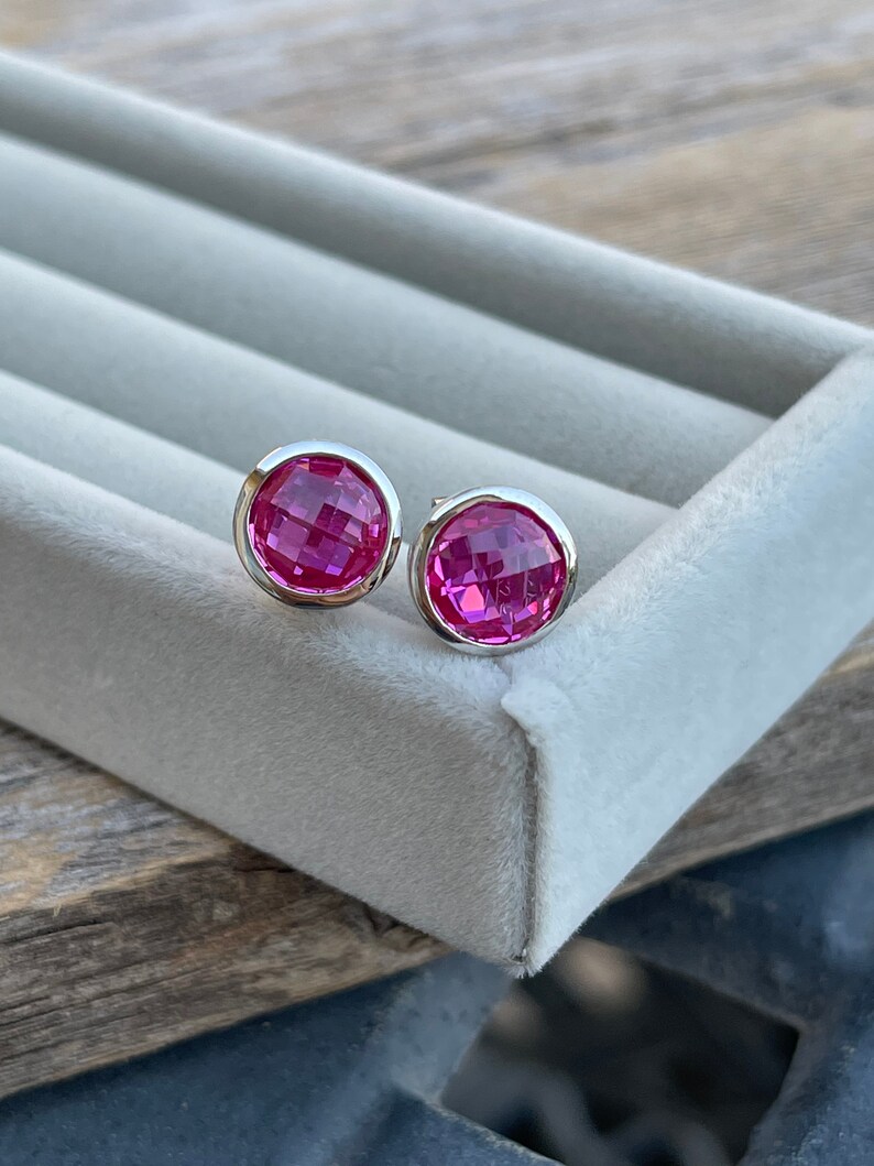 Puede incluir: Un par de pendientes de bot&oacute;n de plata con piedras preciosas facetadas de color rosa.