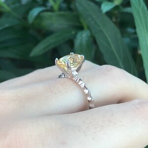 May include: A silver ring with a large, yellow gemstone set in a prong setting. The band is textured and has a delicate design.