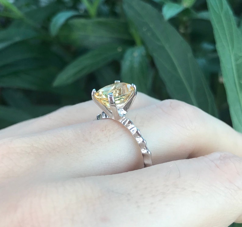 May include: A silver ring with a large, yellow gemstone set in a prong setting. The band is textured and has a delicate design.
