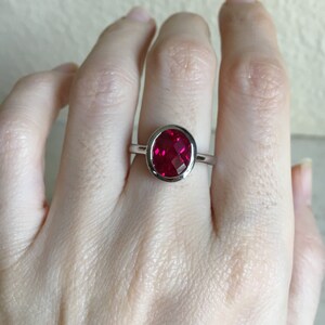 May include: A silver ring with a bezel setting featuring a large, round, red gemstone.
