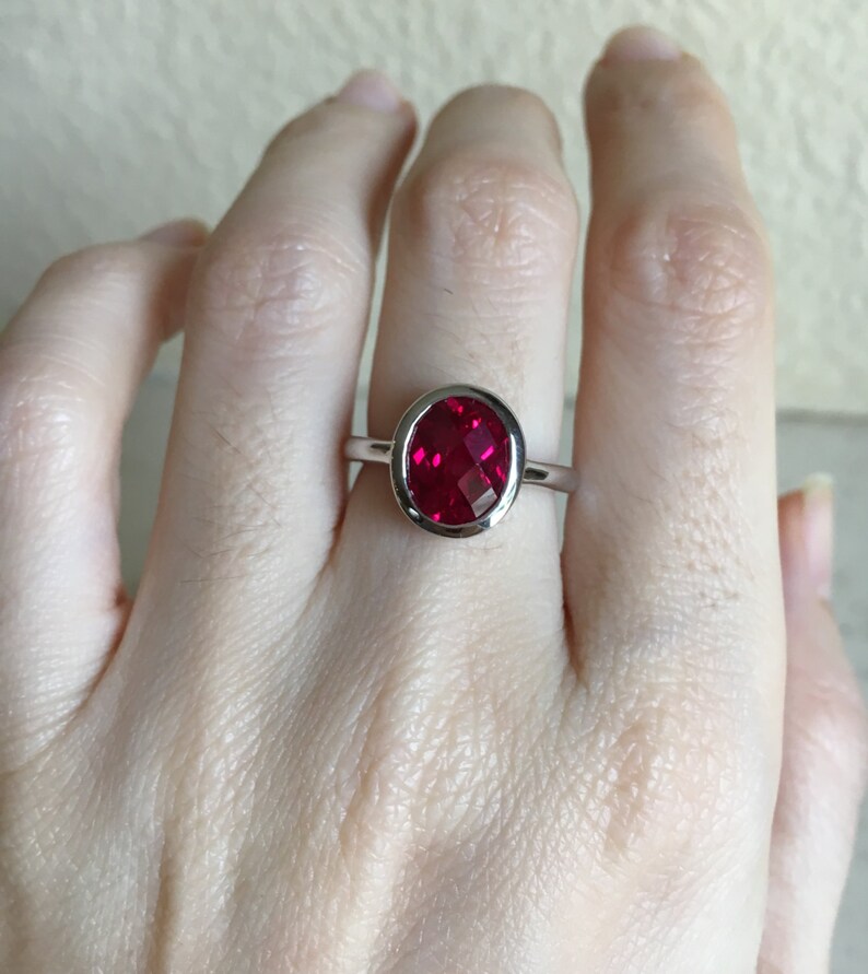 May include: A silver ring with a bezel setting featuring a large, round, red gemstone.