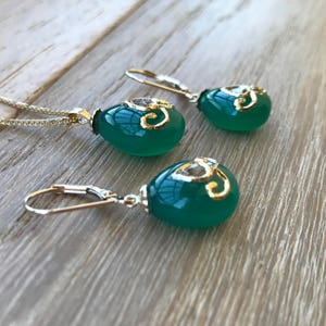 Op de afbeelding: Een ketting met een groene edelsteen hanger en bijpassende oorbellen met gouden accenten en een helder kristal. De hanger en oorbellen zijn traanvormig.