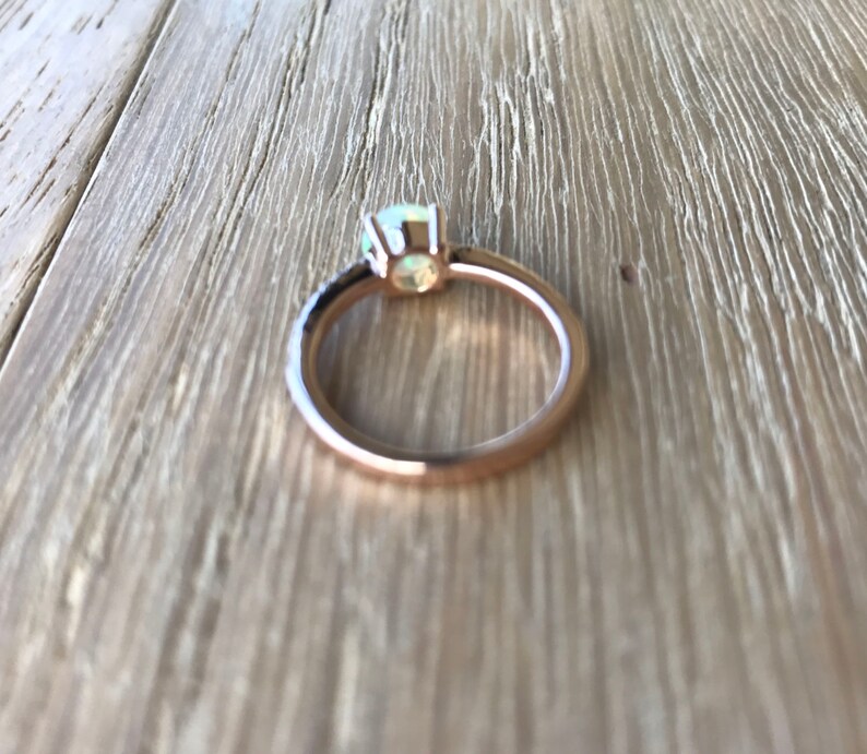 Pode incluir: Um anel de ouro rosa com uma pedra de opala branca e diamantes negros engastados em pav&eacute;.