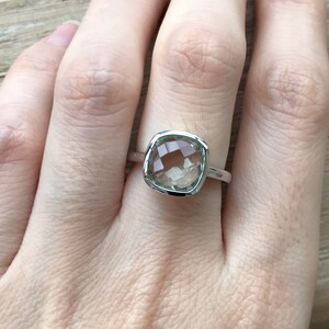 Puede incluir: Un anillo de plata con una piedra preciosa cuadrada de color verde claro.