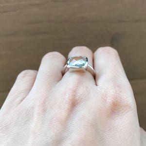 May include: A silver ring with a clear, faceted gemstone. The ring is on a person's finger.