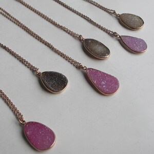 May include: Five gold necklaces with teardrop-shaped pendants made of pink and gray agate. The pendants are all different sizes and shapes.