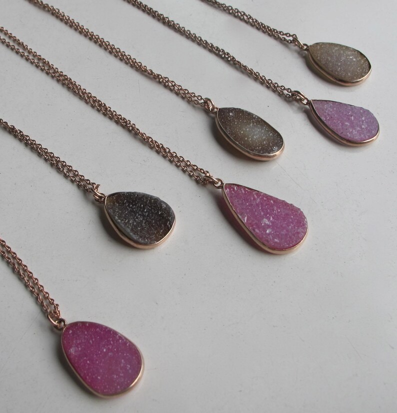 May include: Five gold necklaces with teardrop-shaped pendants made of pink and gray agate. The pendants are all different sizes and shapes.