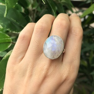 May include: A silver ring with a large oval moonstone. The moonstone is iridescent and has a white, blue, and gray color.