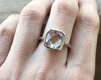 May include: A silver ring with a clear, faceted, square-shaped gemstone.