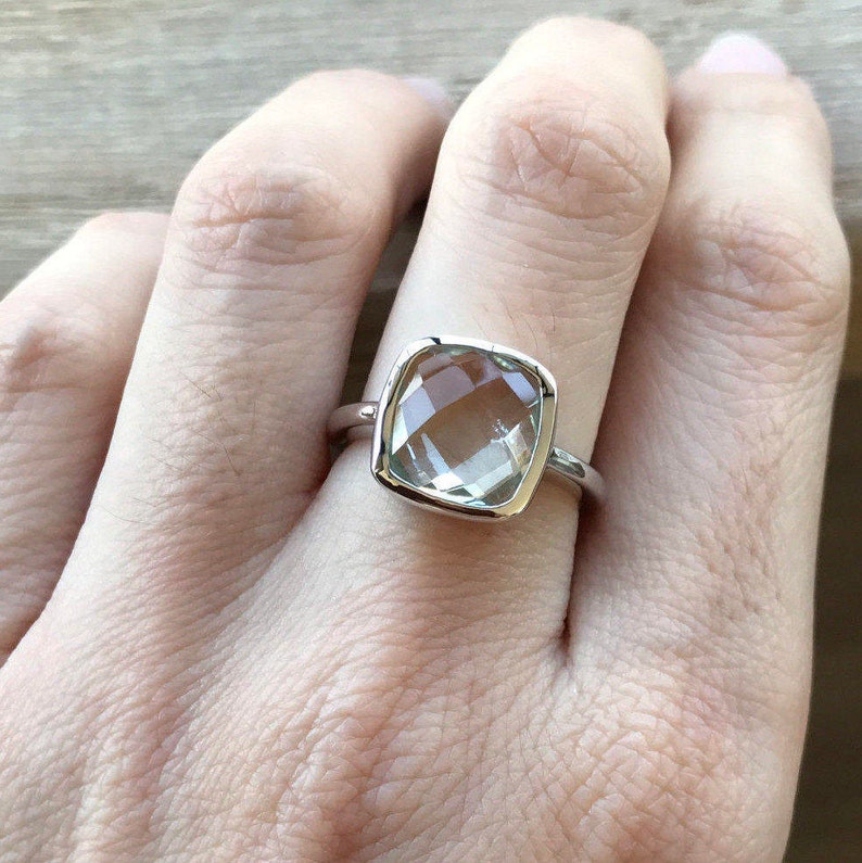 May include: A silver ring with a clear, faceted, square-shaped gemstone.