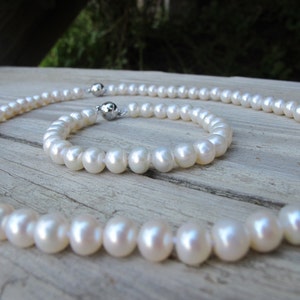 May include: A set of white pearl jewellery, comprising a necklace and a bracelet. The pearls are strung on a silver chain with a magnetic clasp.
