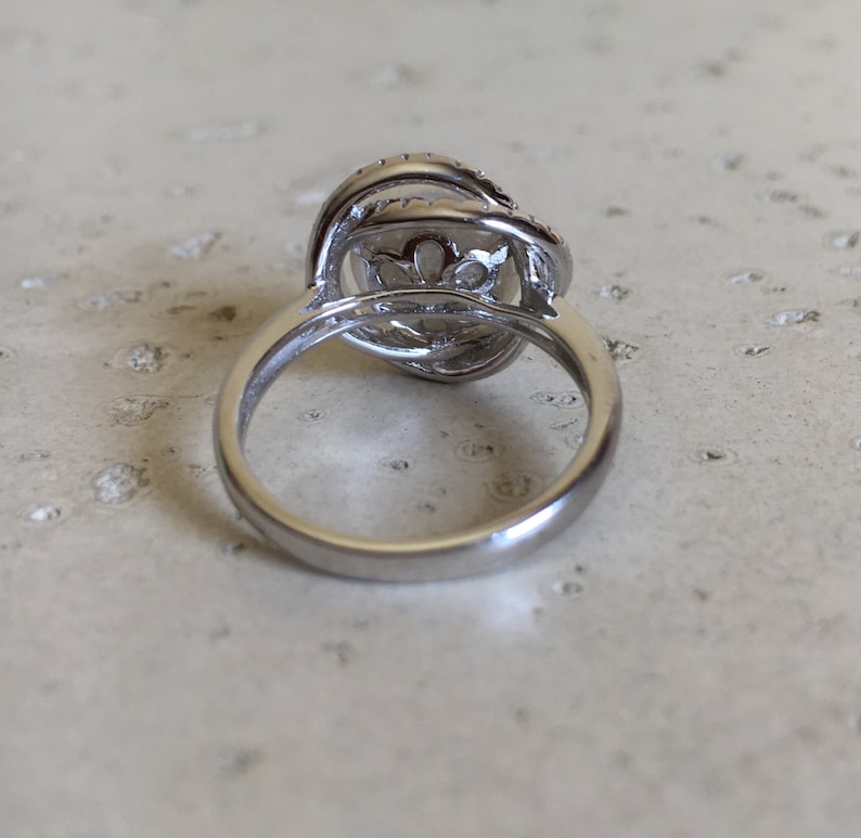 May include: A silver ring with a large, round, clear stone set in a delicate, intricate design. The stone is surrounded by smaller, clear stones.