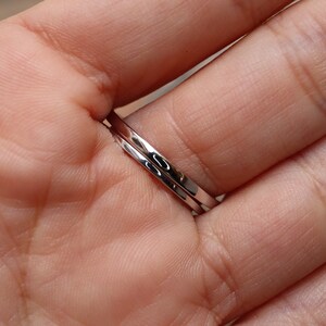 May include: Two silver rings stacked on a finger. The rings are thin and have a smooth, polished finish.