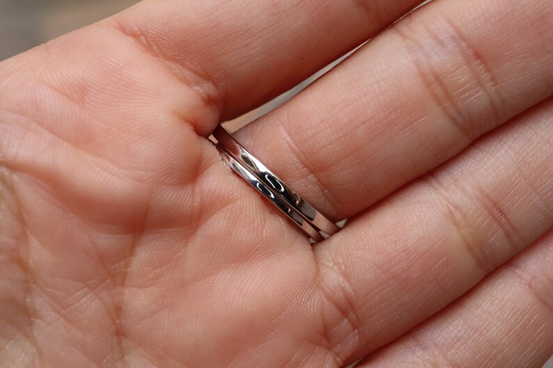 May include: Two silver rings stacked on a finger. The rings are thin and have a smooth, polished finish.