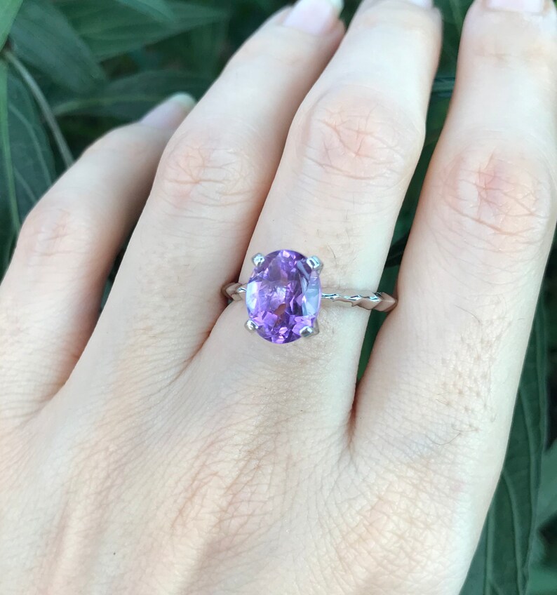 May include: A silver ring with a large oval amethyst gemstone. The ring has a twisted band.