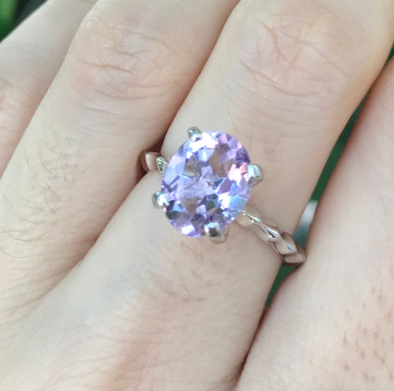 May include: A silver ring with a large oval-shaped amethyst gemstone. The ring has a twisted band.