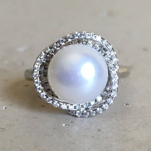 May include: A silver ring with a large white pearl surrounded by a double row of small sparkling diamonds.